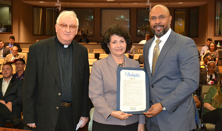 Archbishop Edward McCarthy High School Principal Richard Jean accepts the recognition on behalf of the school from Broward County Commissioner Lois Wexler as Father Brendan Dalton, supervising principal, looks on.