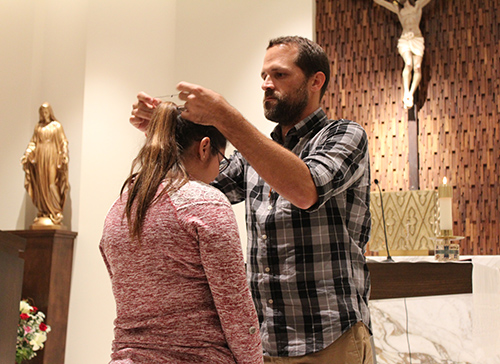 Andres Novela, the mission leader this year, places a wooden cross on Alina Turmo, one of the missionaries going with him to Haiti. Every year, each of the missionaries is given this cross, made by artisans in northwest Haiti.