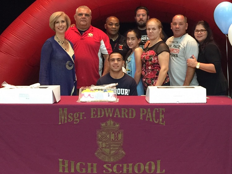 Msgr. Edward Pace High School wrestler Alex Perez poses for a photo with his family, coaches, and Pace Principal Ana Garcia (first on left) after signing a letter of intent to wrestle for Missouri Baptist University.