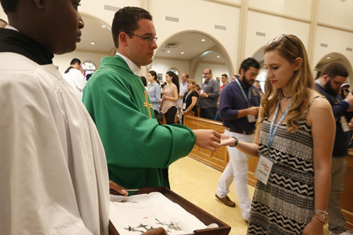 Father Bryan Garcia, parochial vicar at St. Andrew in Coral Springs and one of four priest-chaplains on the official archdiocesan pilgrimage to World Youth Day, distributes pilgrim crosses to World Youth Day pilgrims from throughout the Archdiocese of Miami.