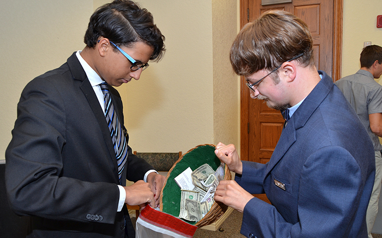 Gabriel Grove, right, adds the contents of his collection plate to the rest of the offering, held by fellow  St. Bonaventure usher Chris Dixon.