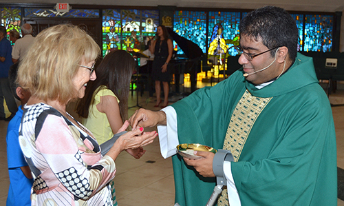 Father Biju Vells distributes Communion at St. Pius X, with help from a crutch.
