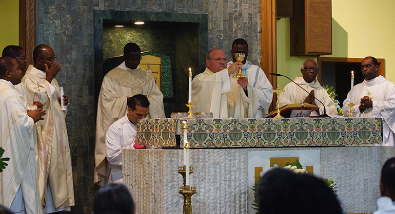 Auxiliary Bishop Peter Baldacchino consecrates the Eucharist during Mass at St. Helen. In attendance were the church's administator, Father Lucien Pierre, center left, and Haitian priests from other parishes in the archdiocese.