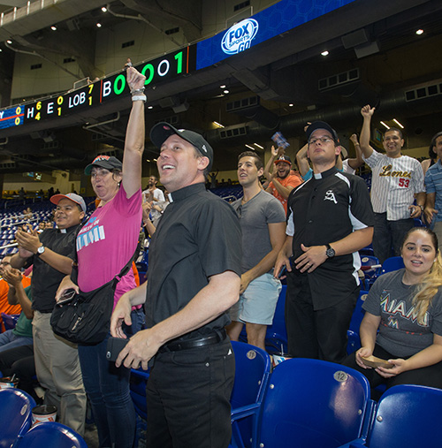 Rosemarie Banich, director of the archdiocese's Office of Youth and Young Adult Ministry, left, and Father Richard Vigoa, the archbishop's secretary, cheer as the Marlins score a run.