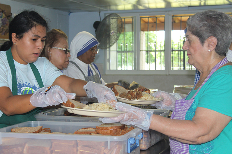 Los voluntarios de las Misioneras de la Caridad sirven la comida para los desamparados. Diariamente se sirve un promedio de 300 platos. A la izquierda la voluntaria Johana Vargas coloca el pan en los platos que la voluntaria Marta María Gómez-Cortes sostiene para los desamparados.