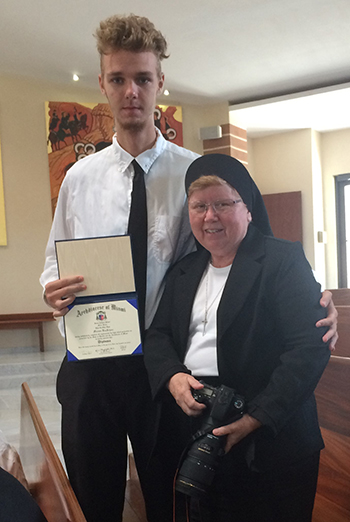 Sister Elizabeth Worley, archdiocesan chancellor for administration, presents the ADOM Virtual Catholic School diploma to high school graduate Marnus Vanschoor of Holy Family Academy.