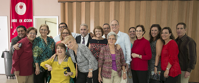 "The old guard," or founding members of Amor en Acción, pose for a photo during the reception. Alicia Marill is seated, fourth from left; hugging her is Gloria Alfonso, who invited Marill to speak at one of the weekly Cursillo meetings she hosted; and right behind Alfonso is Adriano García, whose encounter with Marill that day set the stage for the creation of Amor en Acción.