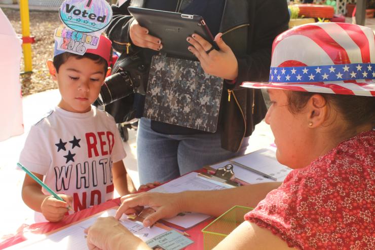 Regístrese aquí: La mamá voluntaria y trabajadora electoral, Maides Infante ayuda a un estudiante de la escuela St. Michael the Archangel, a registrarse para votar en las elecciones de las galletas de la escuela.