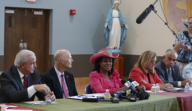El gobernador de La Florida, Rick Scott (segundo desde la izquierda), preside una mesa redonda, el  21 de octubre, en un salón de la catedral, para discutir sobre un nuevo brote de casos de Zika, en el área de Little River, donde se encuentra la Catedral St. Mary. Con él se encuentran, desde la izquierda, el alcalde del Condado Miami-Dade, Carlos Giménez; la congresista estadounidense, Frederica Wilson; la asistente del alcalde del Condado Miami-Dade, Alina Hudak; y el administrador de la ciudad de Miami Beach, Jimmy Morales.