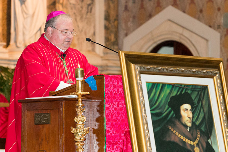 Behind a painting of St. Thomas More, patron saint of lawyers, Auxiliary Bishop Peter Baldacchino delivers his homily to members of the Miami Catholic Lawyers Guild gathered at Gesu Church Oct. 26 for their annual Red Mass.