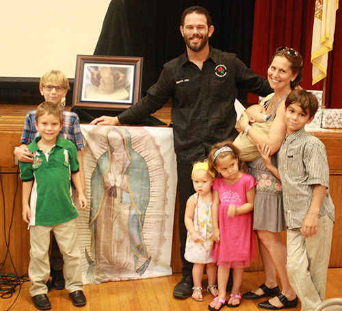 Deacon John Clarke and wife, Dawn, pose in front of an image of Our Lady of Guadalupe with their children, from left: Maximus Florian, 7, Levi Angelo, 5, Willow Maria, 1, Sadie Helena, 3, Jedidiah Paul, 10 weeks, and Elvis Patrick, 9. The Clarkes practice Natural Family Planning and were married 11 years before starting their family. “We had a couple of beautiful surprises… We always said we wanted five,” said Deacon Clarke. Sadie was named in honor of his first date with his wife, who asked him to the Sadie Hawkins dance. They dated all four years of high school.