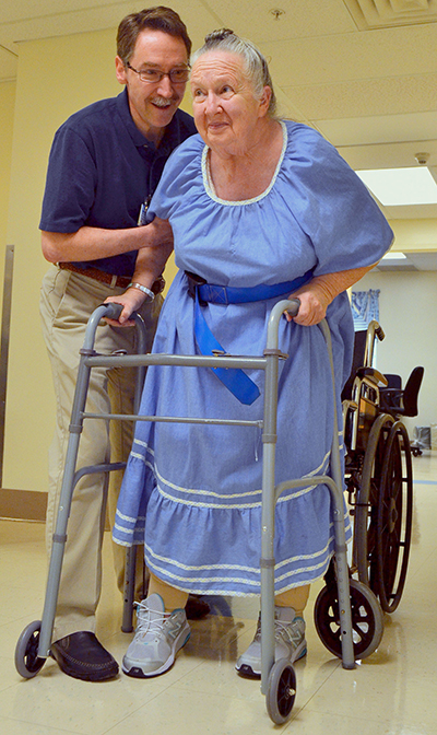 Physical therapist assistant Randal Koerner helps Judy Winters out of her wheelchair onto a walker.