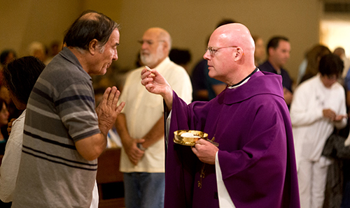 Father Tomasz Grysa, a Polish priest visiting from New York, distributes Communion during the Mass which Miami Archbishop Thomas Wenski celebrated Nov. 26 at Our Lady of Charity National Shrine (La Ermita de la Caridad) in Miami with members of the Cuban community.