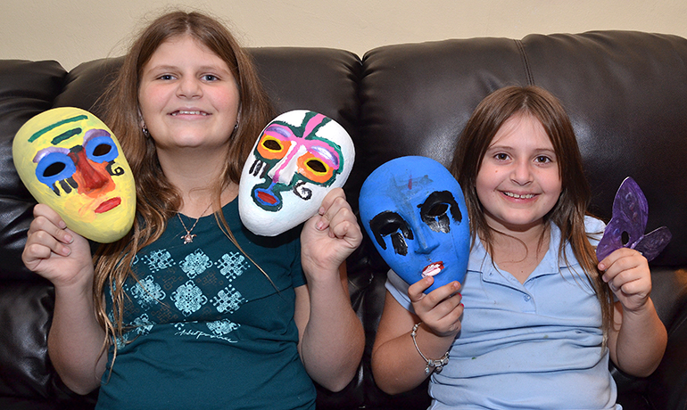 From left are Daley Eisenmann-Byerly, 13, and sister Kailey, 7. They're showing the masks they painted for Camp Erin, symbolizing their emotions.