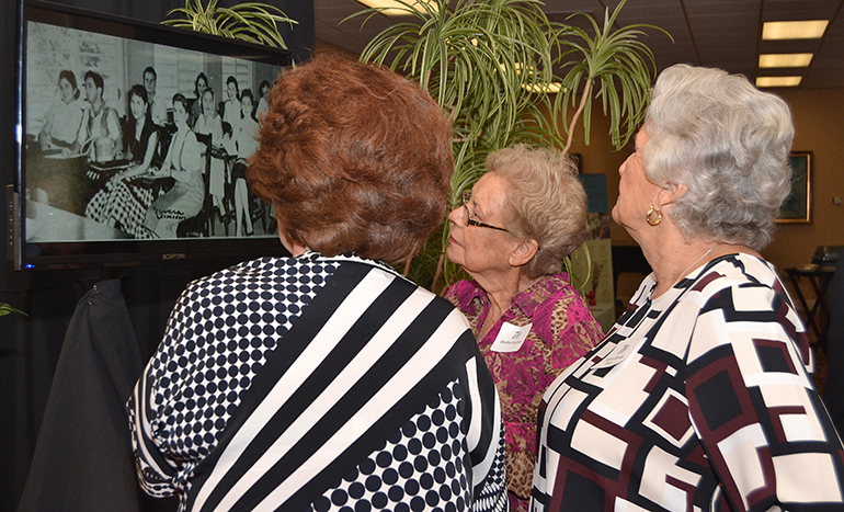 Some alumni gather to watch slide shows of historic photos at the 70th anniversary reception for St. Thomas University.