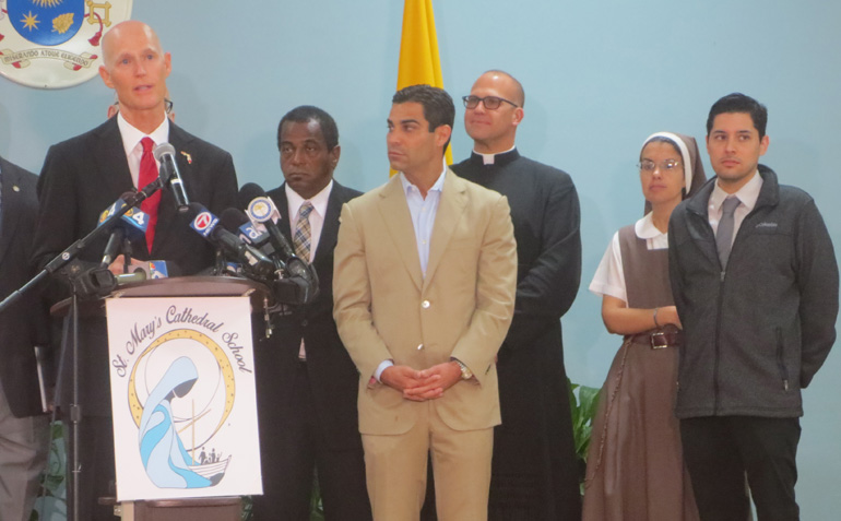 Fla. Gov. Rick Scott speaks at a press conference held at St. Mary Cathedral School Dec. 2, where he announced that the Little River area had been ruled clear of the Zika virus. Also in the photo, from the center right, are Father Christopher Marino, the rector of St. Mary Cathedral, Sister Michelle Fernandez, of the Servants of the Pierced Hearts, principal of the school, and Juan Di Prado, media coordinator of the Archdiocese of Miami.