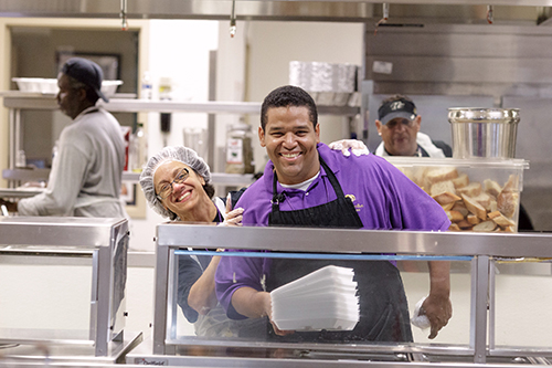 En esta foto de archivo de 2016, Eva Quesada, voluntaria de Camillus House, y Carlos Martinez, miembro del personal de la cocina, se reían en el comedor del centro.