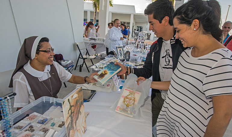 Sister Sonia Mancuello, of the Servants of the Pierced Hearts of Jesus and Mary, sells religious items to Armando and Maria Martinez outside Our Lady of Guadalupe Church in Doral.