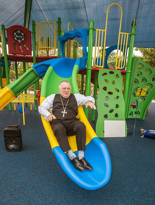 Archbishop Thomas Wenski tries out one of the slides on the play structure of the Sister Lucia Sport and Fitness Park at the Marian Center.