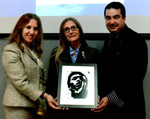 At the opening reception for her exhibit, "Responsibility and Vigilance, A Visual Essay," Susan Buzzi, center, is presented with a smaller copy of one of her works. Buzzi is accompanied by Lawrence Treadwell, STU Library director, and Dr. Roza Pati, director of the Human Trafficking Academy at STU's School of Law.
