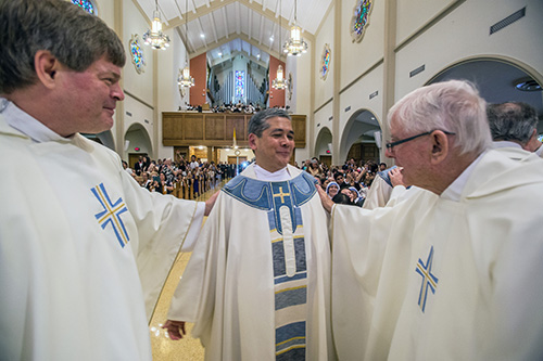 El P. Steven O'Hala, a la izquierda, y Mons. Seamus Doyle, a la derecha, ayudan al recién ordenado P. Edgardo "Gary" De Los Santos a vestirse con sus túnicas sacerdotales. "Él es el que inició todo", dijo el P. De Los Santos sobre Mons. Doyle, su antiguo párroco en St. Rose of Lima, en Miami Shores. Del P. O'Hala, párroco de St. David, en Davie, el nuevo sacerdote dijo: "Puedo verme en él".