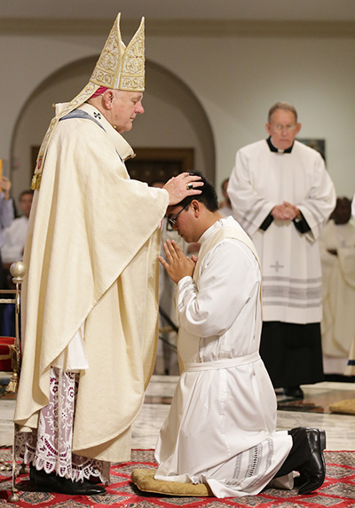 Archbishop Thomas Wenski lays hands on James Arriola, ordaining him to the archdiocesan priesthood.