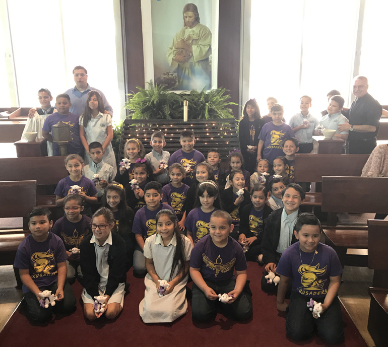 St. Michael the Archangel School students pose for a group photo with their plush lambs given as a first Communion and reconciliation gift to remind them that they are part of Jesus's flock. Also in the photo is St. Michael's director of religious education, Alfonso Balmaceda (rear left), and St. Michael's pastor, Father Francisco Diaz (rear right).