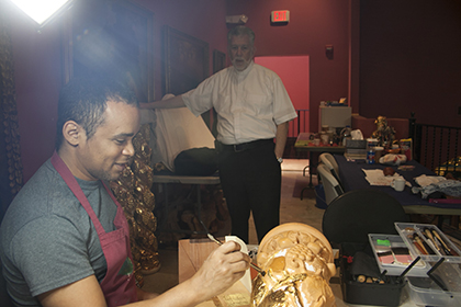 El P. José Luis Menéndez, párroco de Corpus Christi observa como Alexis Caser, especialista en pan de oro coloca las láminas de oro en una columna de madera de cedro tallada, en la Iglesia-Museo La Merced.