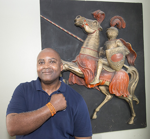 Vonley Williams, Archbishop Curley-Notre Dame class of 1986 and now a resident of Plantation, poses in front of a relief of the school mascot, a Knight. The orange bracelet says, "We are A.C.N.D."