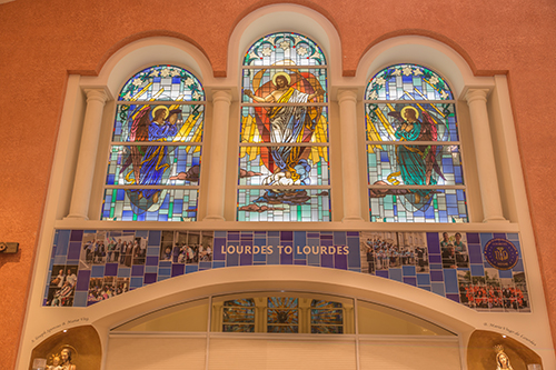 Banner above the main altar of Our Lady of Lourdes Church in Miami includes images of pilgrims from the parish serving the sick in the sanctuary in Lourdes, France.