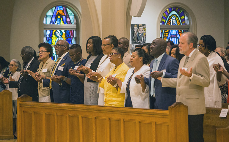 Miembros de la clase de ministros laicos en Creole oran el Padre Nuestro durante la Misa de graduación.