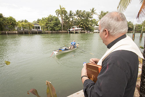 Father Roberto Cid, pastor of St. Patrick, Miami Beach, watches as Greg Dougherty sets off from a canal that runs behind the church on the first day of his 1,400-mile sea journey from Miami to New York.