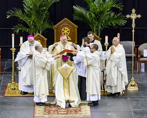 Two deacons, standing at either side, hold the Book of the Gospels above Bishop-elect William Wack's head as Archbishop Thomas Wenski recites the prayer of consecration. Archbishop Wenski was the principal consecrator, with co-consecrators Bishop Joe S. Vasquez of Austin and Bishop Daniel R. Jenky, Congregation of Holy Cross, of Peoria.