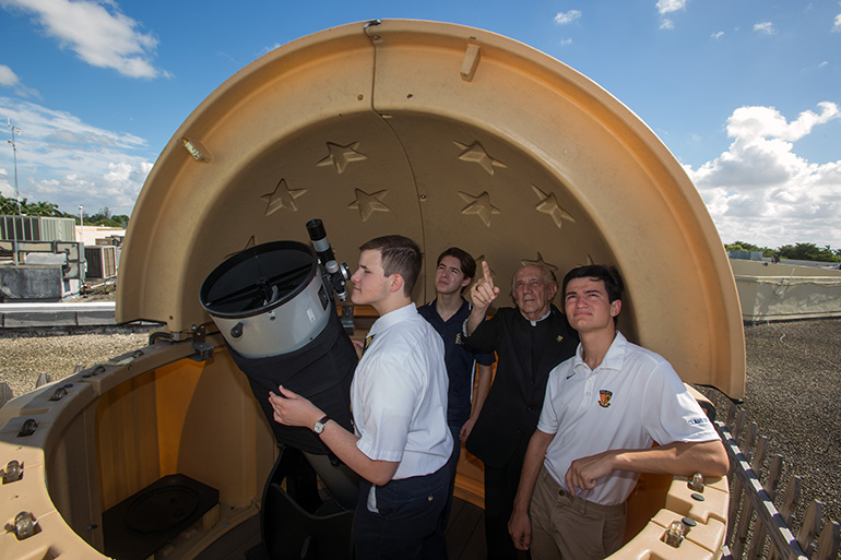 Kevin Galego, 17, gazes through a 12" telescope on a Belen Jesuit rooftop as Danny Jimenez, 14, Jesuit Father Pedro Cartaya and alumnus Michael Cairo, 19, look skyward. Members of Belen Jesuit Preparatory School's Astronomy Club will use the telescopes to view and document the Aug. 21 total solar eclipse.