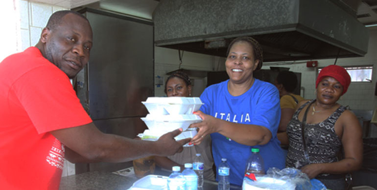 Carline Saintvil hands hot meal to Jean Beaubrun at Holy Family Parish Hall after Hurricane Irma.