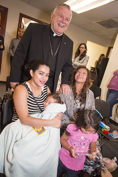 El Arzobispo Thomas Wenski posa con Yosselin y su hija de 2 años, Hadaris, de Honduras, y Erika y su hija Elizabeth, de México, clientes de Catholic Legal Services, durante una visita a las oficinas de la agencia en Miami, el 27 de septiembre, para lanzar la campaña mundial del Papa Francisco "Compartiendo el Viaje" en favor de los migrantes y refugiados.