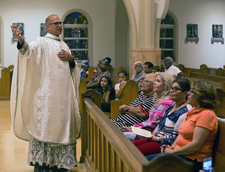 Father Christopher Marino motions toward the statue of Padre Pio which Laura Fabar-Equels, seated in the first row wearing a pink dress, and her husband donated to St. Mary's Cathedral.