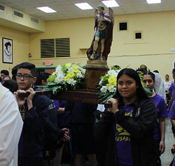 Eighth graders Marcel Gonzalez and Elizabeth Norori carry the image of St. Michael the Angel into the cafeteria at the start of the celebration.