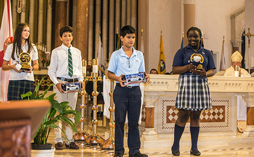 Sunny Isles Police Chief Fred Maas presented two students each from St. Patrick and St. Lawrence schools with gifts during the Blue Mass: police cars for the boys and teddy bears named Freddy for the girls. From left, holding their gifts: St. Patrick seventh grader Carolina Heimes, 12, and eighth grader, Samuel Vasquez, 13; and St. Lawrence eighth grader Julian Quintero, 13, and seventh grader, Leyla Masson, 12.