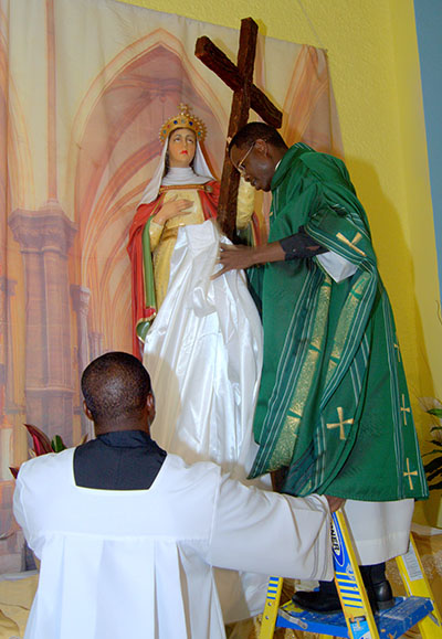 Father Lucien Pierre unveils a new statue of St. Helen during the kickoff Mass for the church's 50th anniversary. Assisting him is seminarian Reynold Brevil.