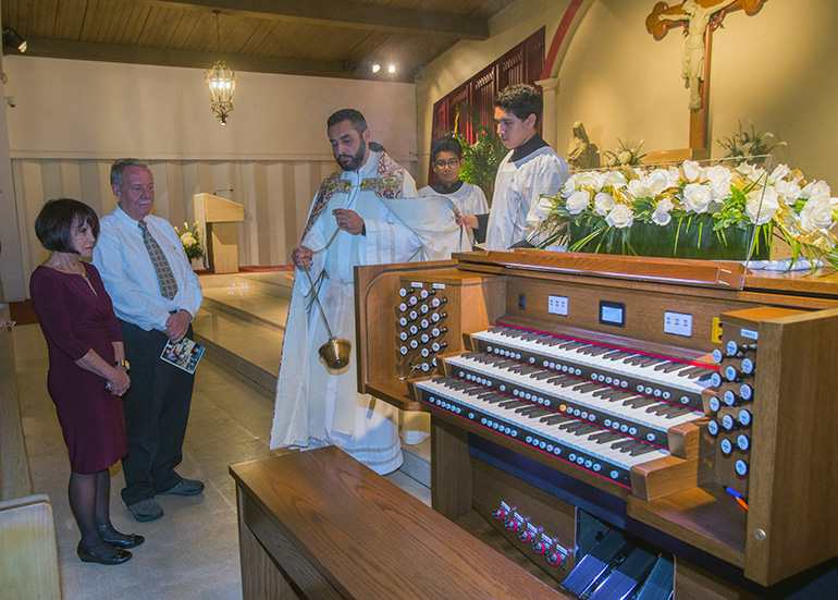 Father Robert Ayala, St. Matthew Church administrator, incenses the new organ which Lucy Vanpelt, mother of Justin Lex Norris, donated to the church in her son's memory. She and Justin's father, Lex Norris, are standing beside the organ.
