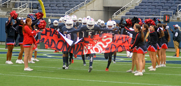 James Williams (5) leads the Chaminade-Madonna Lions through the banner before their 31-28 victory over the West Palm Beach Oxbridge Academy ThunderWolves in the Class 3A FHSAA Football Final Dec. 9 at Camping World Stadium in Orlando. The Lions won their third state championship in school history.