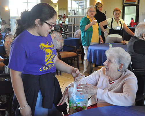 A student member of the Mission Club at St. Michael School gives a Christmas present to a Floridian nursing home resident.