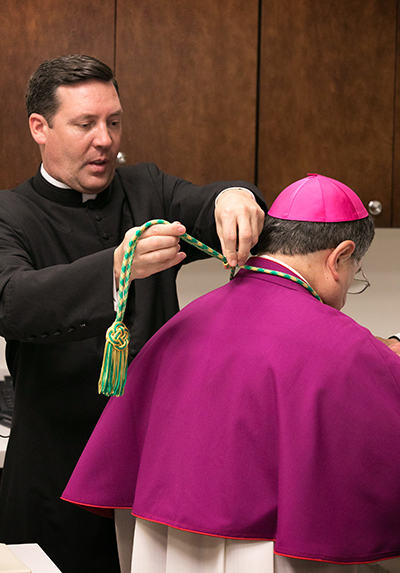 Father Richard Vigoa assists Bishop-elect Enrique Delgado in vesting prior to the start of solemn vespers on the eve of his ordination as the newest auxiliary bishop of the Archdiocese of Miami.