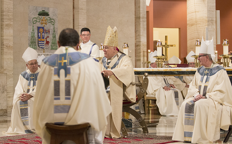 Bishop-elect Enrique Delgado, his back to the camera, listens as Archbishop Thomas Wenski delivers his homily at the ordination Mass. Seated at either side of the archbishop are his co-consecrators, Bishop Felipe Estevez, left, of St. Augustine, and Bishop John Noonan of Orlando, both former archdiocesan priests.