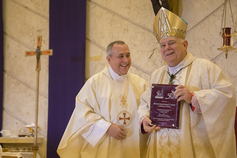 El P. José Álvarez, párroco de la iglesia Our Lady of the Lakes, le entrega al Arzobispo Thomas Wenski una placa para conmemorar el Jubileo de Oro de la parroquia, el 8 de diciembre.