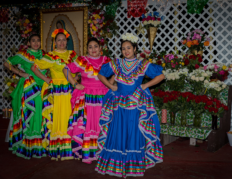 De izquierda a derecha: Vanesa Lagunas, Isabel Nuñez, Raquel Arriada, and Anadeisy Aguirre, vestidas con atuendos folklóricos, se preparan para bailar en honor a la Virgen de Guadalupe.