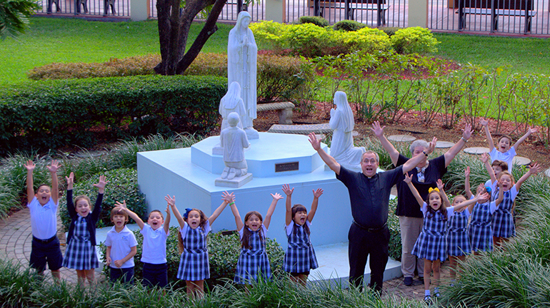 "¡Hiiiiiiii!" Los niños de kindergarten de la escuela Our Lady of the Lakes se reunieron alrededor de la estatua de la Virgen de Fátima con el P. José Álvarez, párroco de la iglesia. Detrás de él esta Irma Tejeda, feligresa de toda la vida y maestra de kíndergarten.