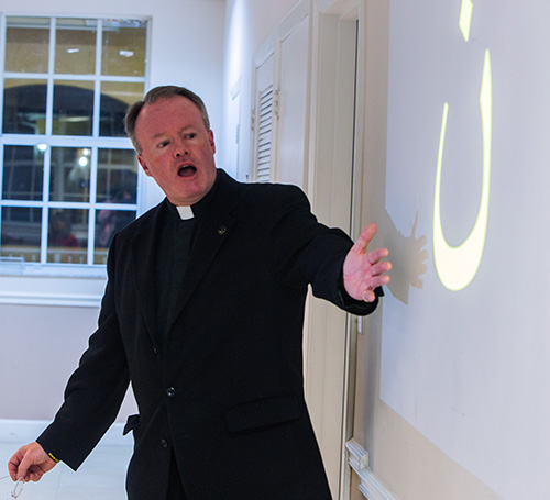 Father Benedict Kiely points to the Arabic symbol for the letter N, Nazarean, which was painted in Christian homes to identify them for martyrdom by ISIS. The priest spoke Dec. 11, 2017 at St. Agnes Church, Key Biscayne, about the persecution of Christians in the Middle East.