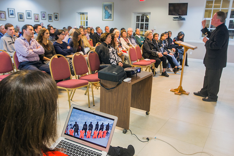 Father Benedict Kiely addresses the audience as a slide presentation is shown, with Coptic Christians about to be martyred by beheading by Islamic terrorists. The priest spoke Dec. 11, 2017 at St. Agnes Church, Key Biscayne, about the persecution of Christians in the Middle East.